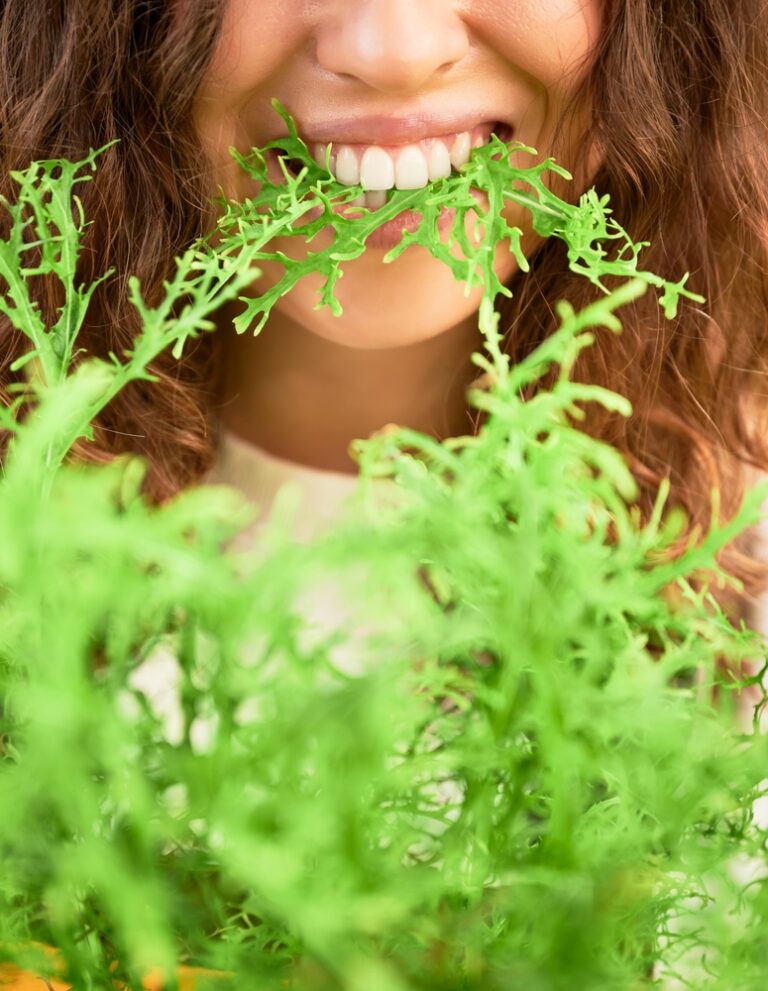 grøn mizuna der spises af mørkhåret kvinde
